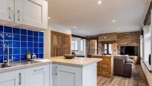 A modern kitchen with white cabinets, a blue backsplash, and a wooden island. - Stable Block (Wimborne)