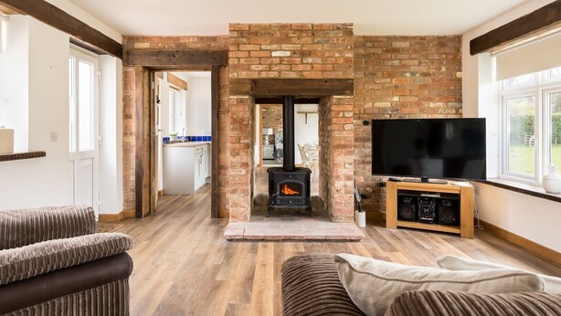 A living room with a brick fireplace, a television, and a sofa. - Stable Block (Wimborne)