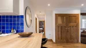 A kitchen with a wooden countertop, a large mirror, and a blue-tiled backsplash. - Stable Block (Wimborne)