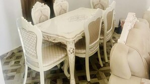 Un coin repas avec une table et des chaises blanches, une porte en bois et un revêtement de sol à motifs.