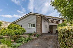 A single-story house with a covered porch, a brick section on the right, and a garden with various plants and flowers.