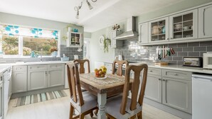 Una cocina moderna con armarios blancos, una mesa de comedor de madera con sillas y un frutero.