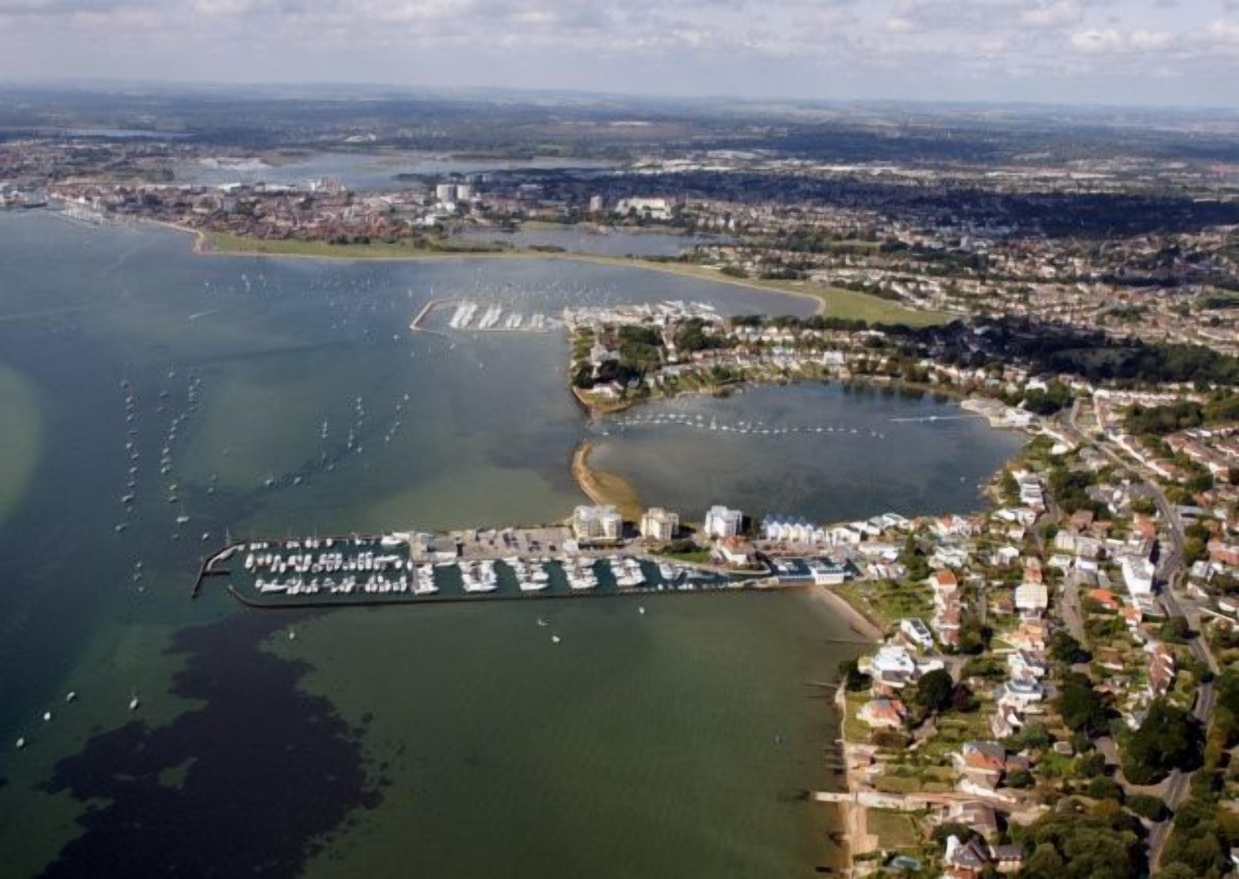 An aerial view of a coastal town with a marina, residential areas, and a large body of water.