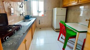 A kitchen with wooden cabinets, a white refrigerator, a gas stove, and a window. - Apartment (fes)