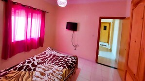 A bedroom with a bed, a television mounted on the wall, and a door leading to another room. - Apartment (fes)