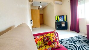 A hotel room with a sofa, a colorful pillow, a television, and a patterned rug. - Apartment (fes)