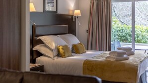 A hotel room with a bed, nightstand, lamp, and a view of greenery through the window.
