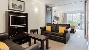 A modern living room with a flat-screen TV, a leather sofa with yellow cushions, a small coffee table, and a framed picture on the wall.