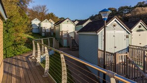A row of small, light-colored wooden cabins with a wooden deck and railing in the foreground.