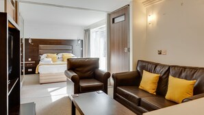 A modern hotel room with a bed, a leather armchair, a sofa, and a small table.