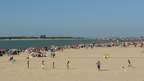 Une plage bondée, où l’on voit des gens se promener et s’amuser, des parasols et un ciel dégagé.