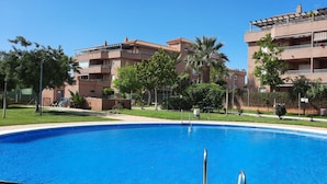Une piscine entourée d’une pelouse bien entretenue et de palmiers, avec des immeubles à plusieurs étages en arrière-plan.