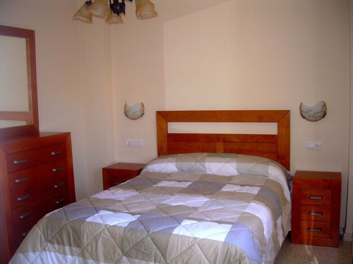 Ein Schlafzimmer mit einem hölzernen Kopfteil, einer gesteppten Bettdecke, zwei Nachttischen und einer Holzkommode.