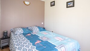 A bedroom with a bed, a bedside table with a lamp, and two framed pictures on the wall. - Le Quiloé - Apt lumineux proche mer (Frontignan)
