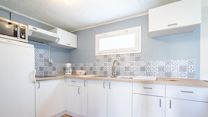 A compact kitchen with white cabinets, a microwave, a sink, and patterned backsplash tiles. - Le Quiloé - Apt lumineux proche mer (Frontignan)