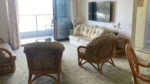 Una sala de estar con un sofá, dos sillones de mimbre, un televisor de pantalla plana y un ventilador de techo.