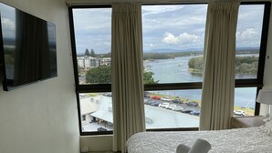 Habitación de hotel con un ventanal que ofrece vistas de un río, edificios y coches aparcados.