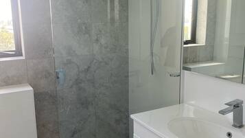 Een moderne badkamer met een douchecabine van glas, een wit wastafelmeubel en een grote spiegel.