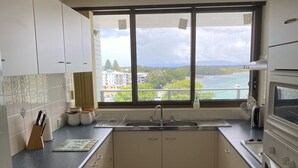 Una cocina con armarios blancos, un ventanal con vista al agua y edificios, un lavamanos y una estufa.