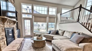 A living room with a stone fireplace, a round coffee table, a beige sofa, and a staircase.