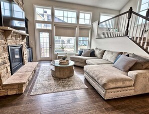 A living room with a stone fireplace, a round coffee table, a beige sofa, and a staircase.