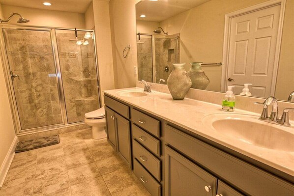 A bathroom with a glass shower enclosure, a toilet, a vanity with a large mirror, and a sink.