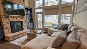 A living room with a stone fireplace, a flat-screen TV, a sofa, and a large window.