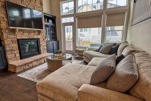 A living room with a stone fireplace, a flat-screen TV, a sofa, and a large window.
