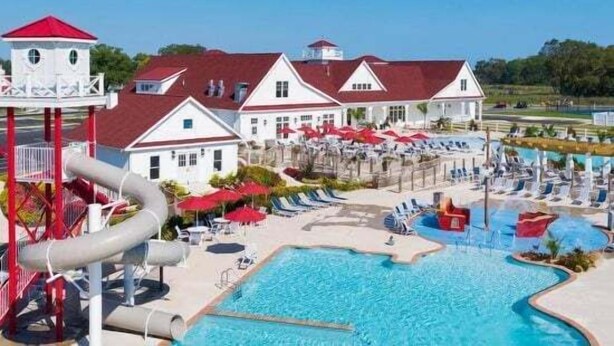 A swimming pool area with a water slide, lounge chairs, and a building with a red roof.