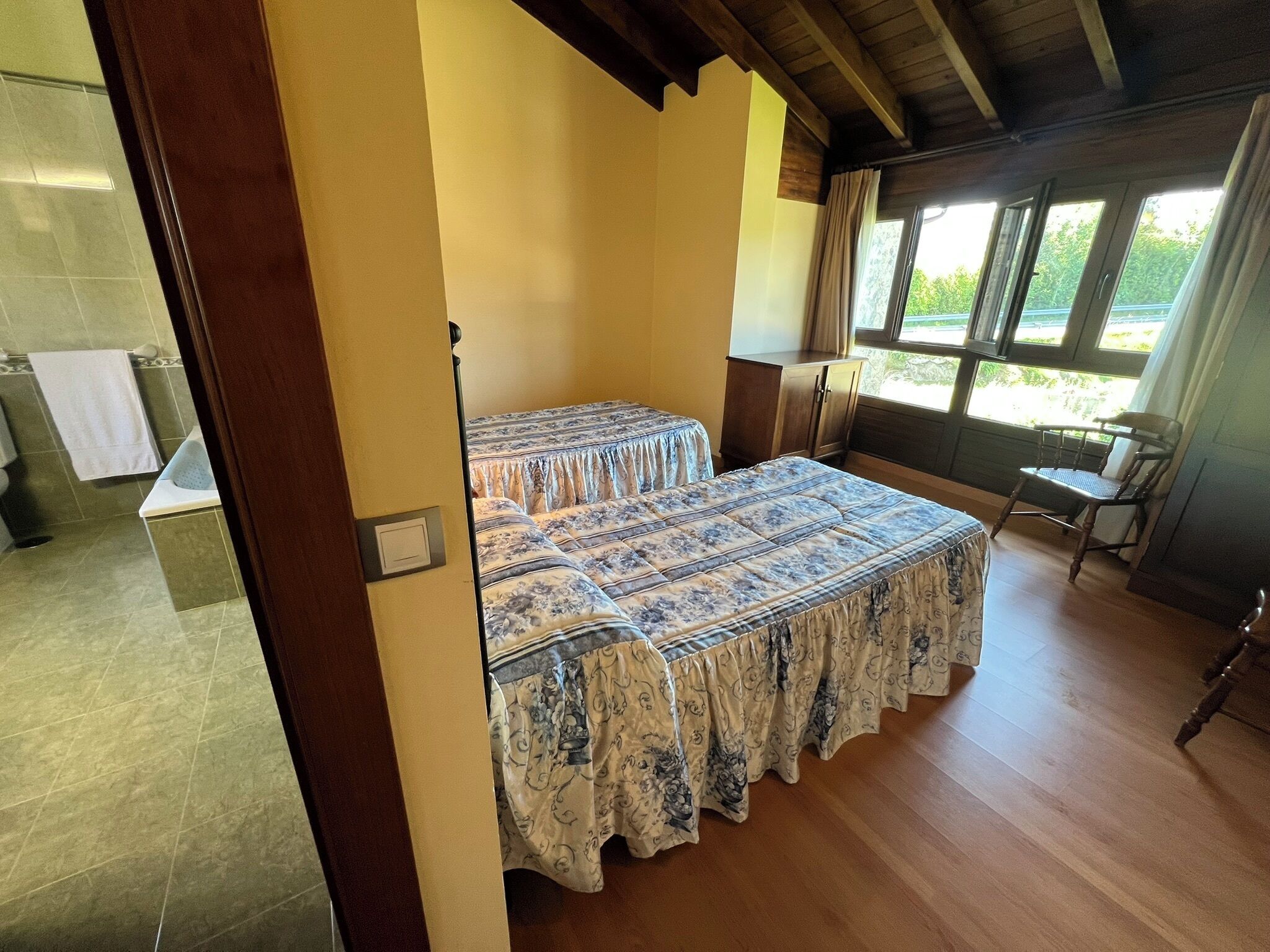 Un dormitorio con una cama, una silla, una ventana y un baño a la vista.