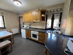 A kitchen with wooden cabinets, a microwave, a coffee maker, a sink, and a dining area with a table and chairs.