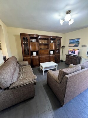 Ein Wohnzimmer mit zwei gemusterten Sofas, einem weißen Couchtisch, einer Holzkabine mit Glastüren, einem Fernseher und einem gerahmten Bild an der Wand.