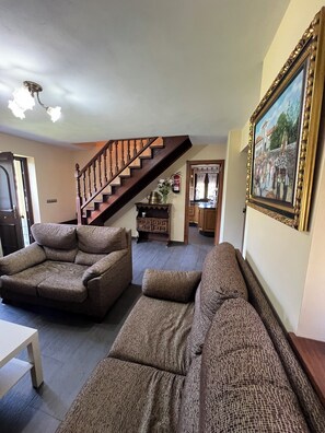 Ein Wohnzimmer mit einer Holztreppe, zwei Sofas, einem Gemälde und einer Küche im Hintergrund.