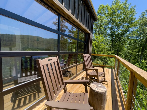 Relax on the deck with a view of the surrounding forest, surrounded by comfortable seating and a small table.