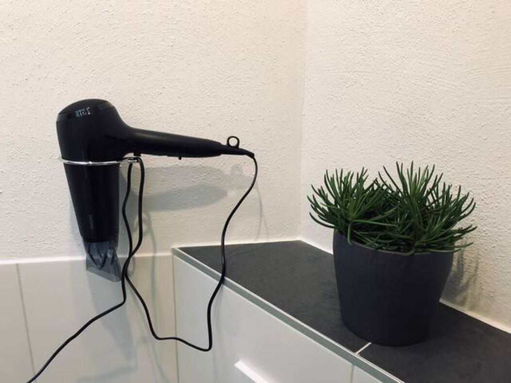 En hårtørrer på en hvid væg, en potteplante og en glasoverflade.