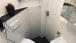 Un baño pequeño y moderno con inodoro, lavamanos y una pequeña planta en maceta sobre el mostrador.