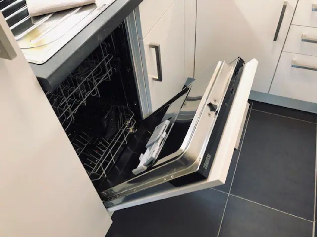 Un four ouvert avec une grille à l’intérieur, un plan de travail blanc et un sol carrelé.