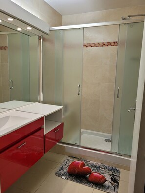 Ein modernes Badezimmer mit einer ein Glasfachwerk-Duschkabine, einem weißen Waschtisch mit roten Schubladen und einem gefliesten Boden.