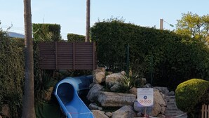 Une piscine avec un toboggan bleu, entourée de rochers, de palmiers et d’un panneau.