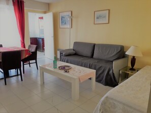 Un salon comprenant un canapé, une table basse, une table à manger avec des chaises et une lampe.