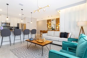 Una sala de estar moderna con sofá, sillas, una mesa de centro y una cocina con electrodomésticos.