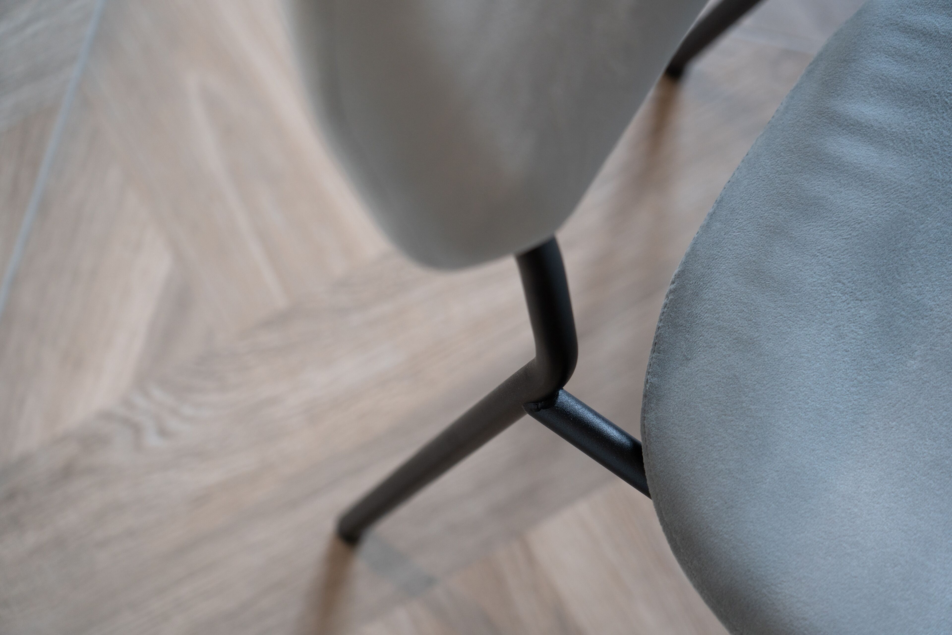En närbild på en stol med en grå tygklädd sits och ett svart metallstativ, placerad på ett trägolv.