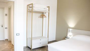 Habitación de hotel con cama, mesita de noche con lámpara, armario con perchero y puerta que da a otra habitación.