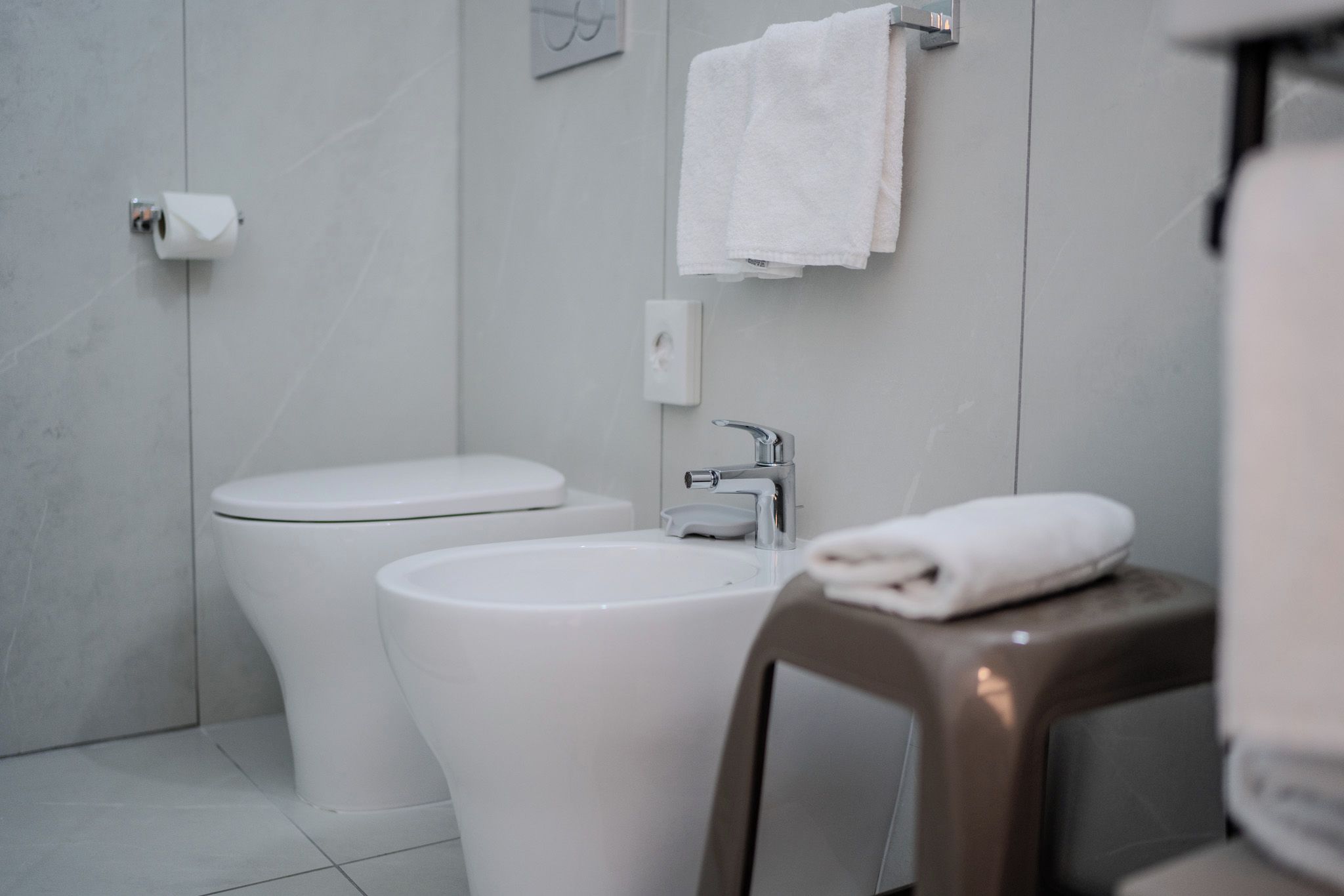 A bathroom with a toilet, sink, and a towel on a stool.