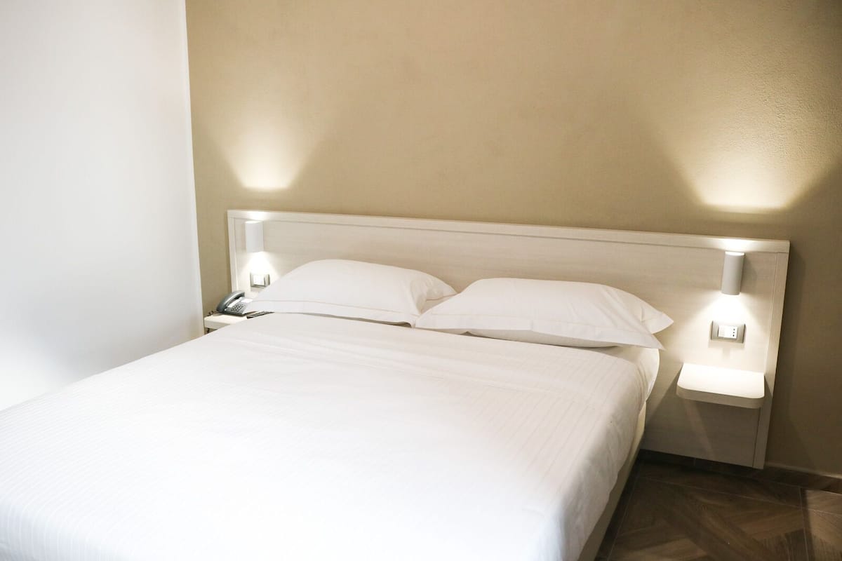 A neatly made bed with white linens in a hotel room.