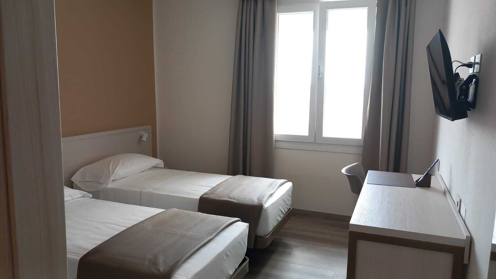Ett hotellrum med två separata sängar, ett litet skrivbord, en stol och en tv som är monterad på väggen.
