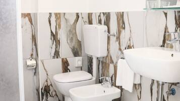 Un bany amb vàter, bidet i rentapel, tot de color blanc. El terra té un dibuix que imita el marbre.