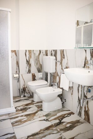 A bathroom with a toilet, bidet, and sink, all in white. The floor has a marble-like pattern.