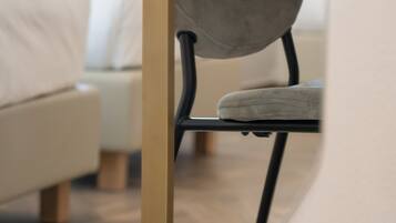 Una silla moderna con estructura metálica y asiento acolchado, ubicada en una habitación luminosa con un ventanal y una cama al fondo.