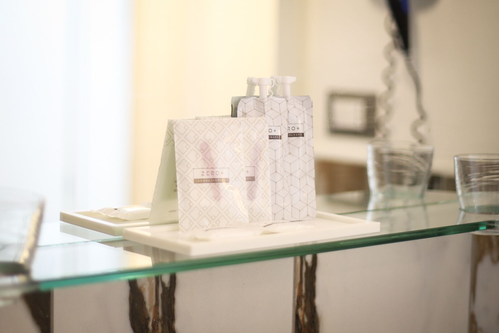 Una mesa de vidrio con tres botellas blancas etiquetadas "ZERO+ AROMATHERAPY" sobre una bandeja blanca.